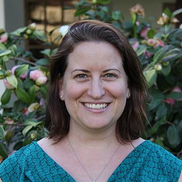 A person smiling in front of greenery. 