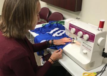 Person sewing on a machine with blue fabric labeled 