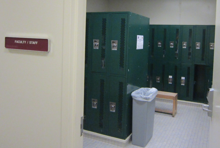 A locker room with green lockers, a bench, and a trash bin.