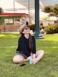 Image of fitness instructor Mx. Monique Moon sitting on grass looking up with her legs crossed