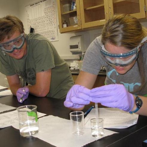 A student uses a pipette in a lab setting, with another student looking on. Links to Environmental Sciences BS page.
