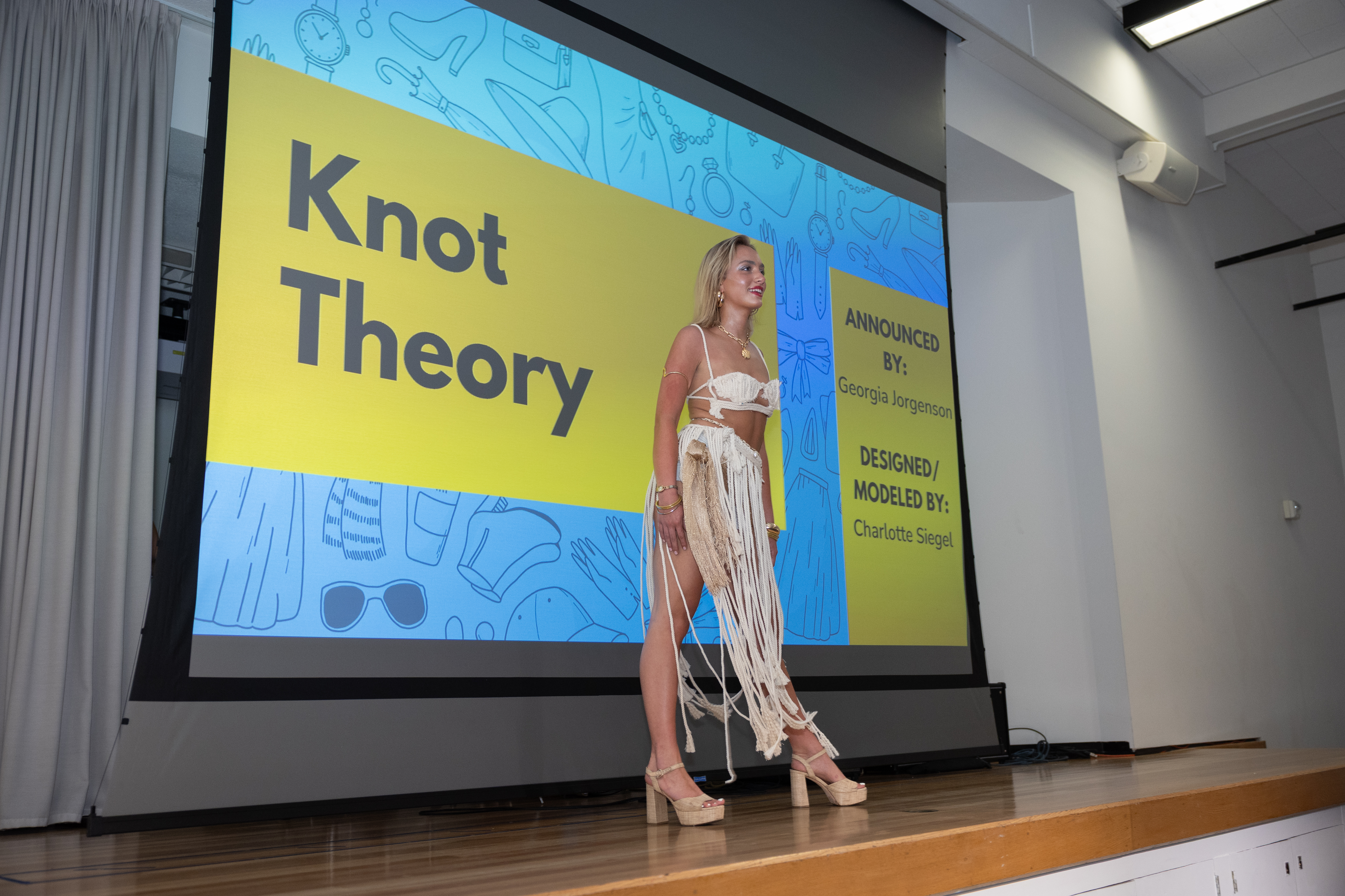 EcoFashion Show 2025: A model a dress made of knotted rope in front of a screen saying Know Theory