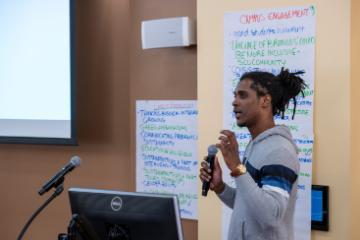 a person speaking into a hand-held microphone in front of a hand-written flip-chart