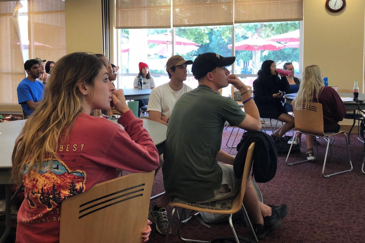 Students sitting at tables looking to the front of the room to listen to a presentation