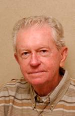 An older man wearing a striped shirt against a plain background.