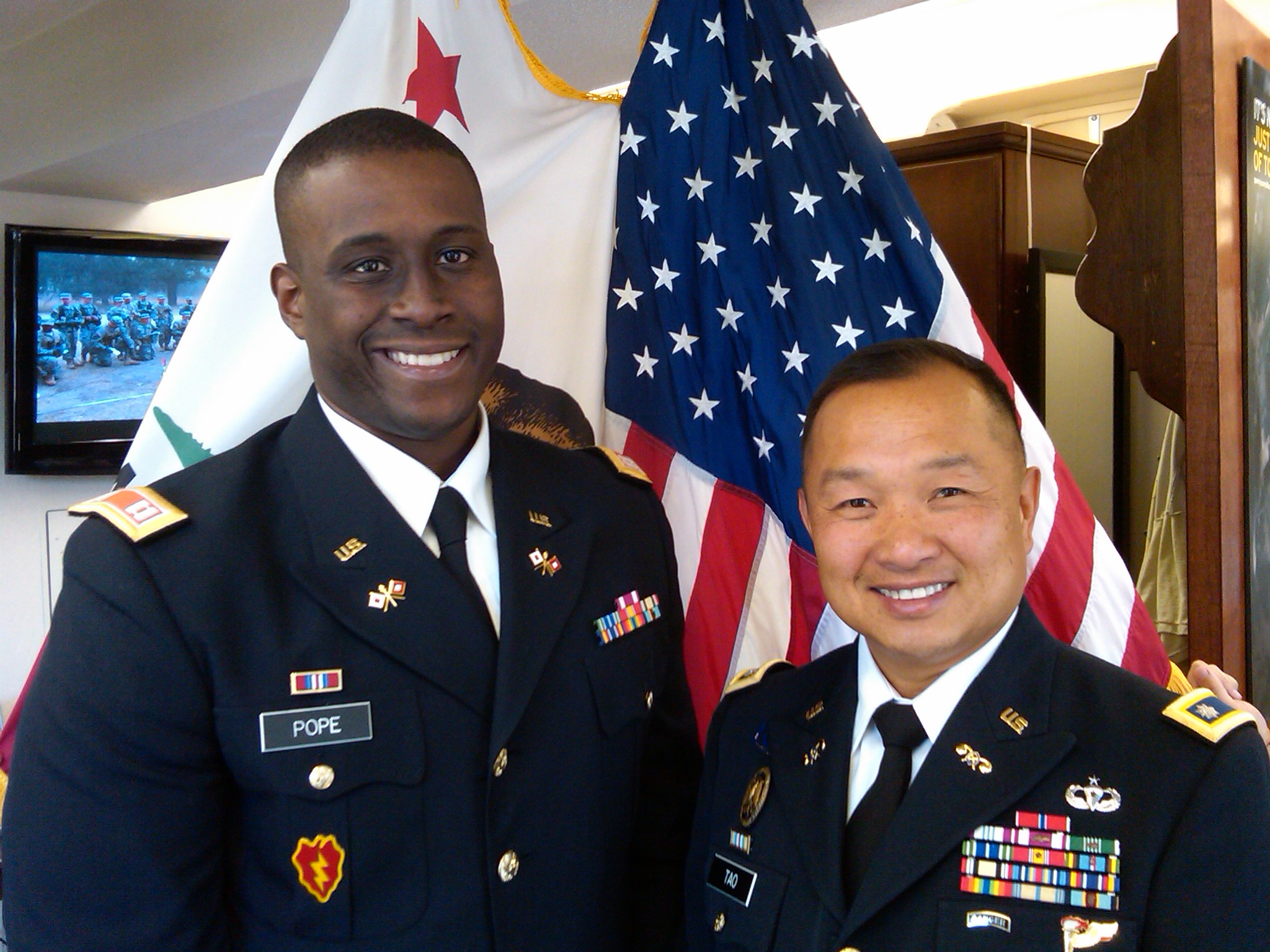 Two military personnel in uniform standing in front of U.S. flags. image link to story