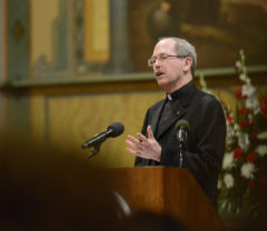 Man speaking at a podium in a church with floral arrangements.