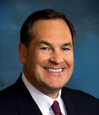 A person smiling in formal attire with a blue background. image link to story
