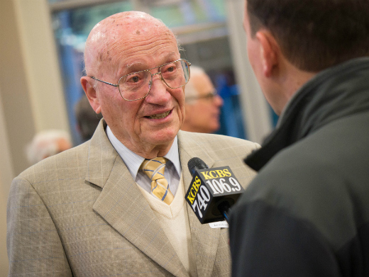 Two people conversing, one in a suit and the other in casual attire. image link to story