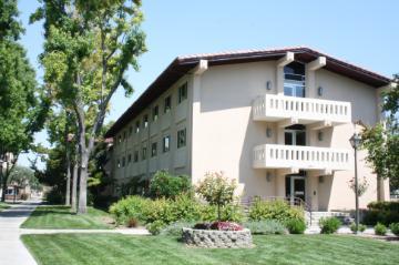Three-story residential building with balconies and surrounding greenery.