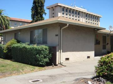 A beige building with plants and bushes in front.