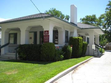 A white building with columns, green lawn, and shrubs.