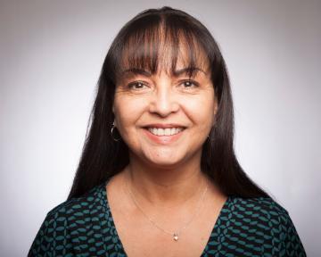 A person smiling in a studio portrait with a light background.