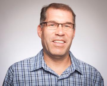 A person wearing glasses and a plaid shirt smiles.