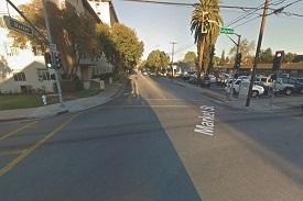 View of a crosswalk on a street with parked cars and trees.