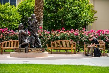 Bronze statues of seated chimpanzee and young chimpanzee on all fours in garden.