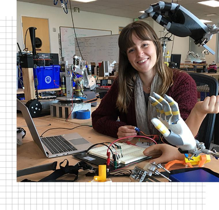 A smiling female student posing before a prosthetic hand