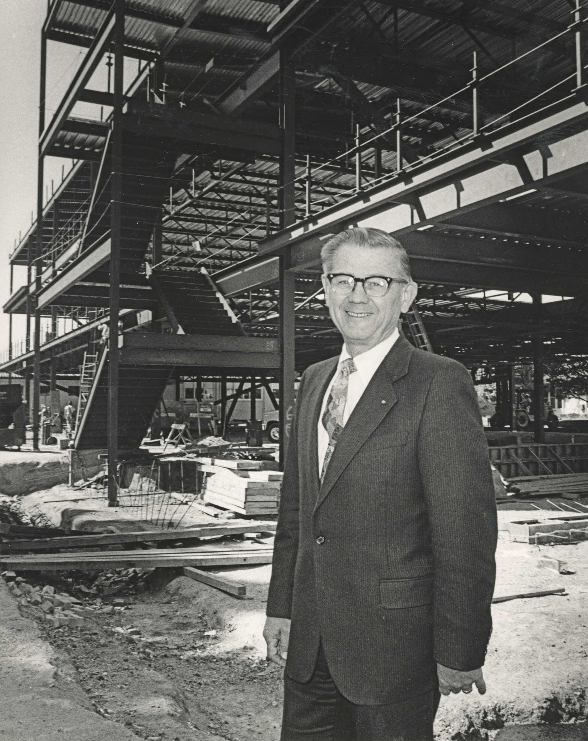 A person in a suit standing in front of industrial machinery.
