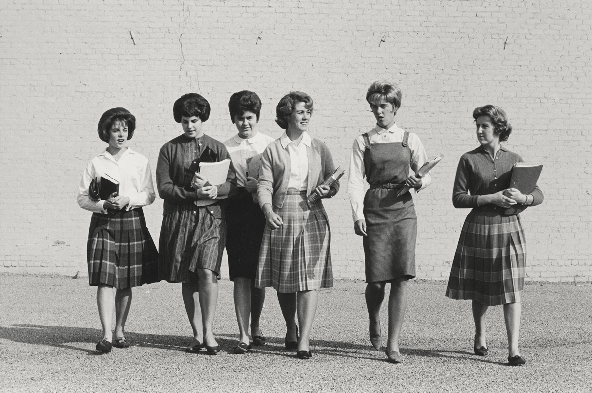 Six women standing in a row, some holding books, in casual attire.