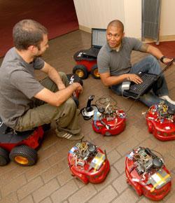 Two people working with multiple small robots on the floor.