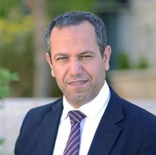 Man in a suit and tie standing outdoors, titled 'Salem Al-Agtash'.