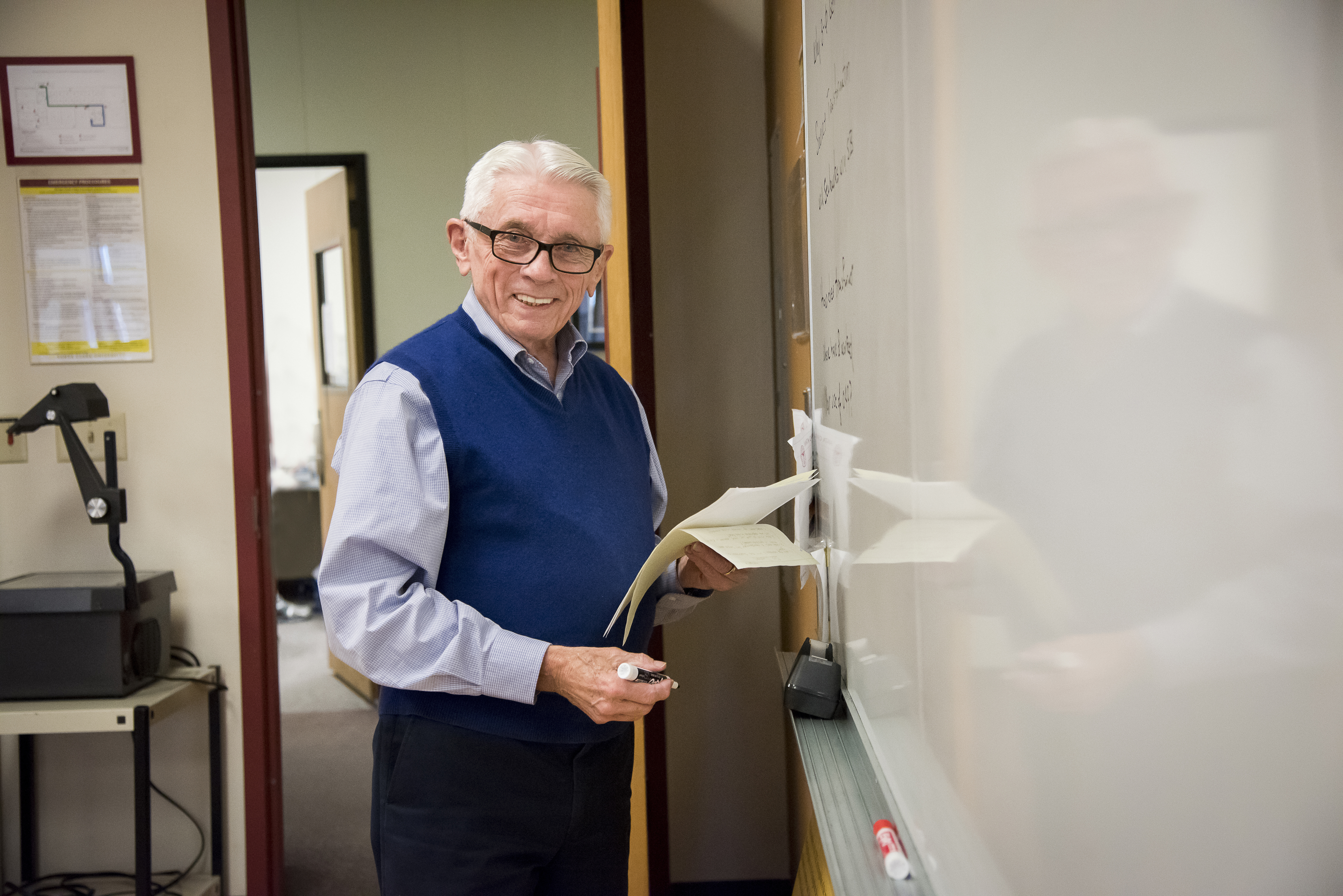 Man in an office walking through a doorway holding a notebook. image link to story