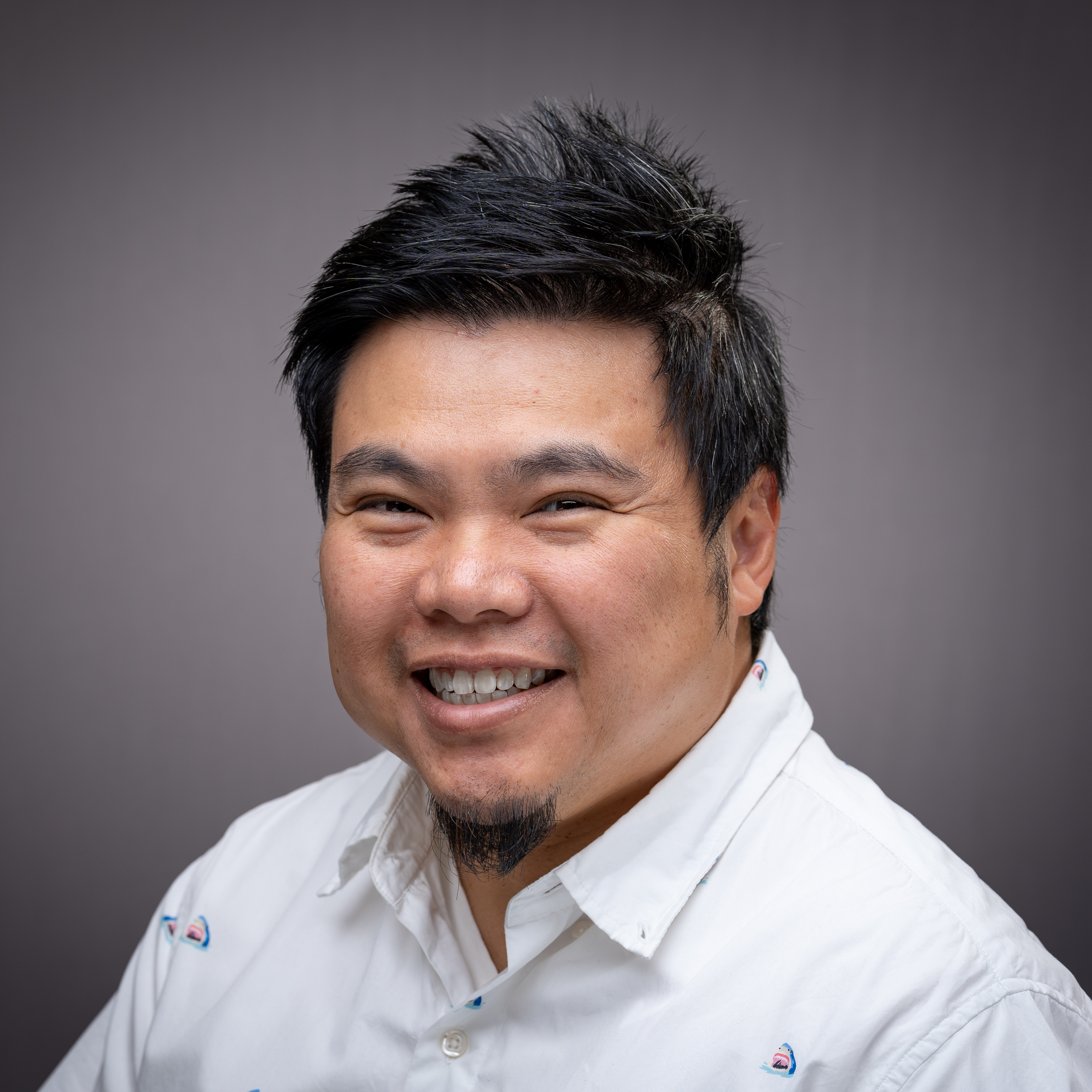 Man in a white shirt smiling against a gray background.