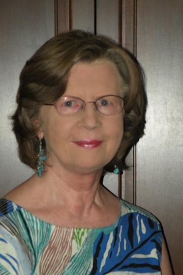 A woman smiles gently, wearing a patterned top.