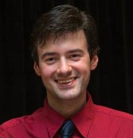 A person smiling in a red shirt with a black background.