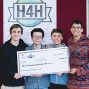 Four happy male students standing in front of a Hack for Humanity sign hold a big check.