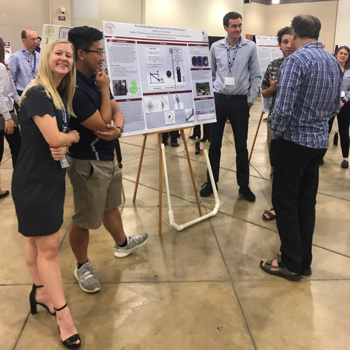 Female student smiles at the camera while male teammate talks about their poster with visitors image link to story