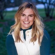 A person smiling outdoors wearing a white vest and blue shirt. image link to story