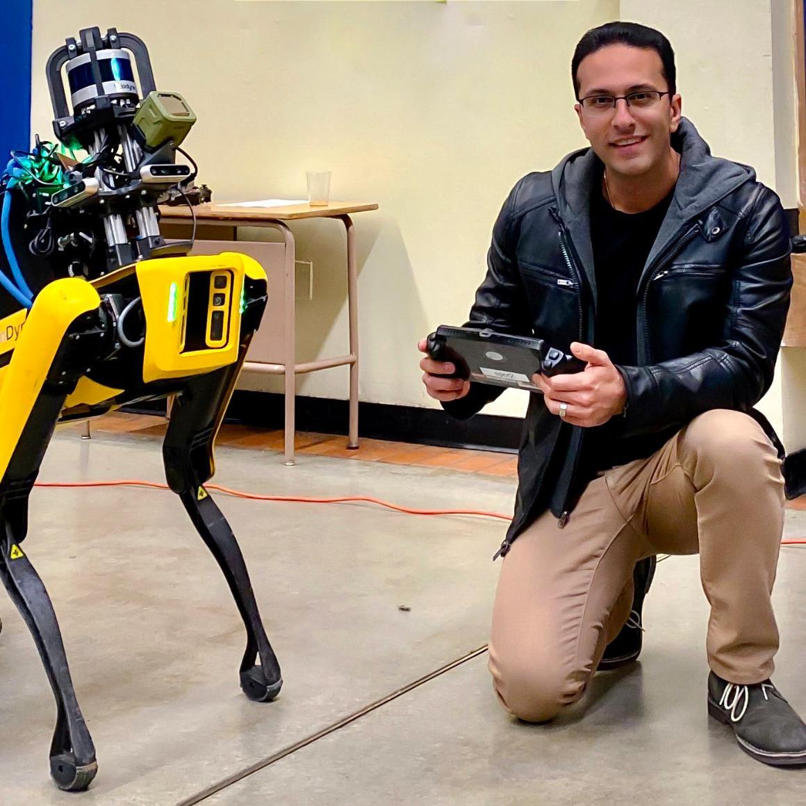 Kamak Ebadi, holding a controller, kneels next to a 4-legged robot