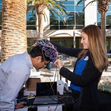 Student Samantha Perez demonstrates the NeuroGen EEG and Near-Infrared Light Stimulation helmet on a Senior Design guest