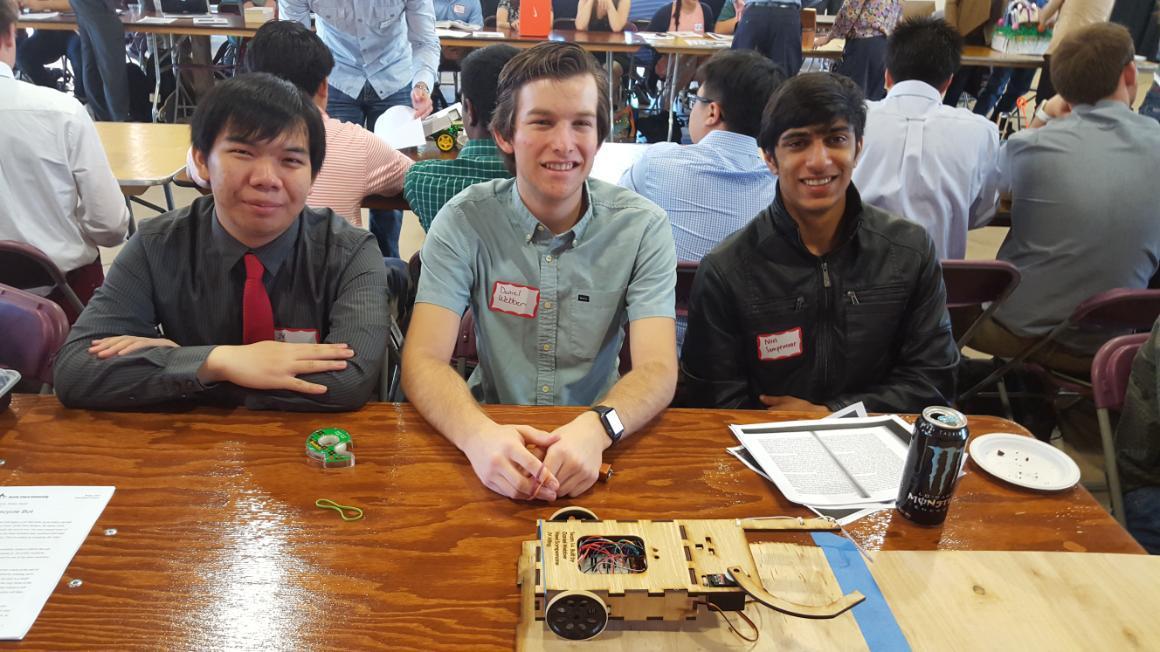 Three people seated at a table with papers, a phone, and a bottle.