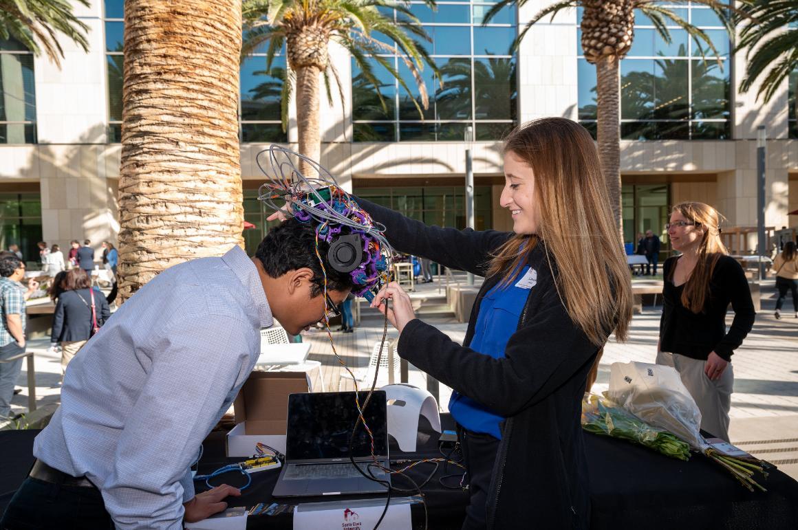 Student Samantha Perez demonstrates the NeuroGen EEG and Near-Infrared Light Stimulation helmet on a Senior Design guest image link to story