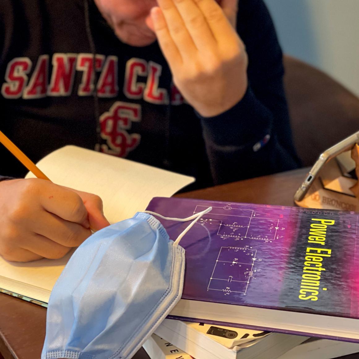 A stressed engineering student working at home with phone, mask, textbooks image link to story