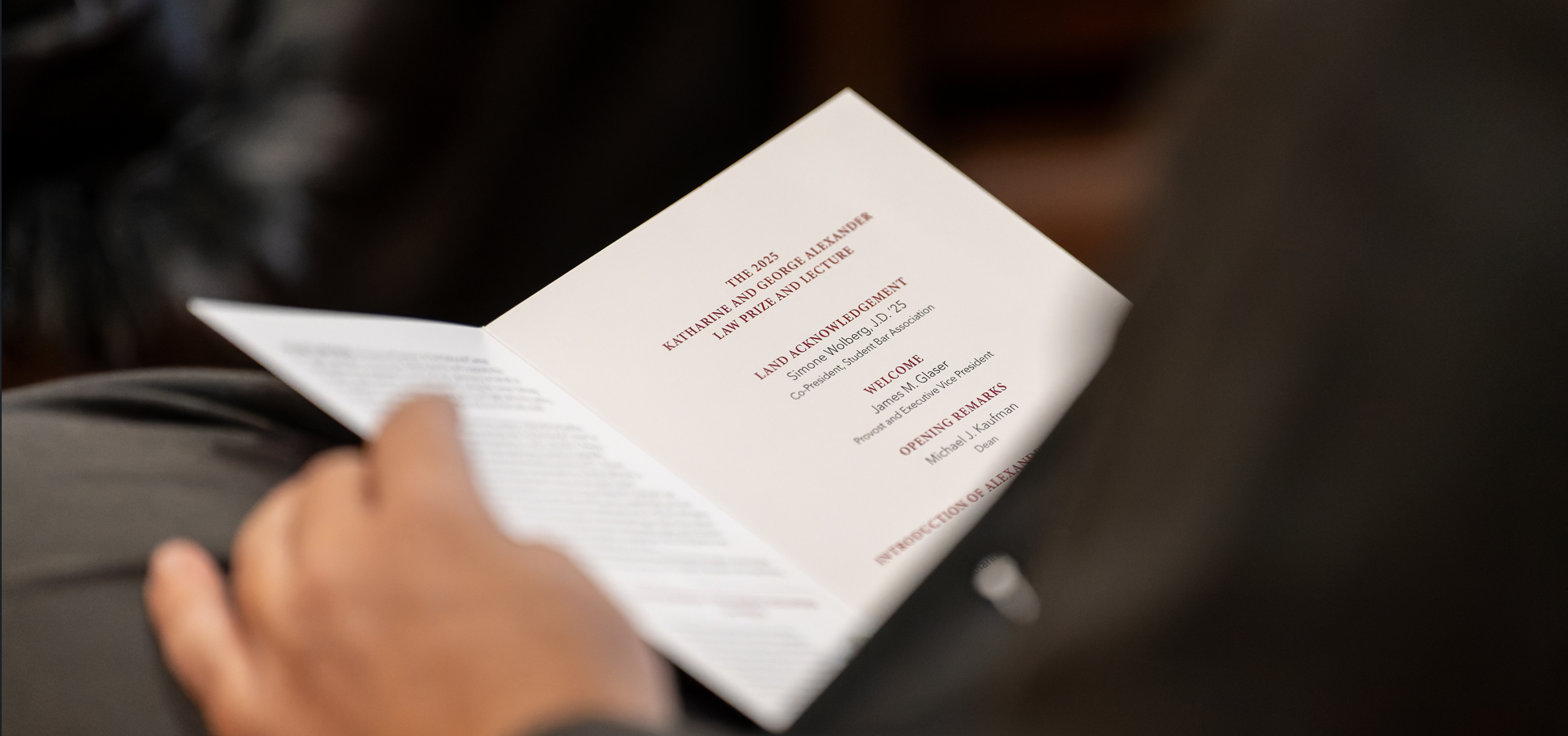 A person holds an open brochure for the 2025 Katharine and George Alexander Law Prize and Lecture.