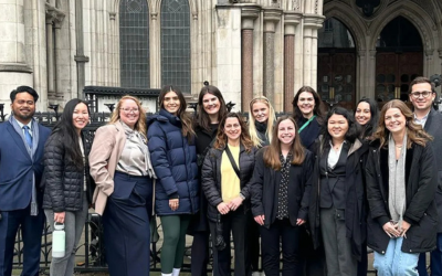 A diverse group of colleagues standing together in front of a historic stone building with large arched doorways. 