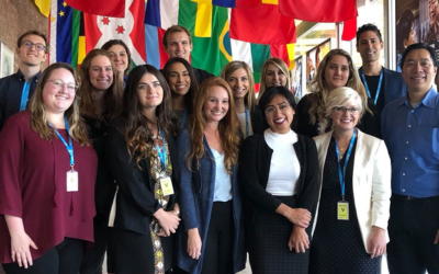 A group portrait of coworkers standing in front of international flags. 